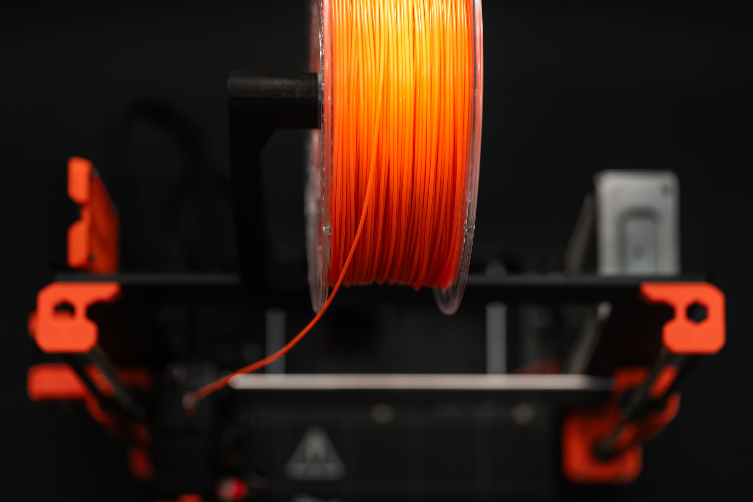 Orange filament spool feeding a 3D printer against a dark background.